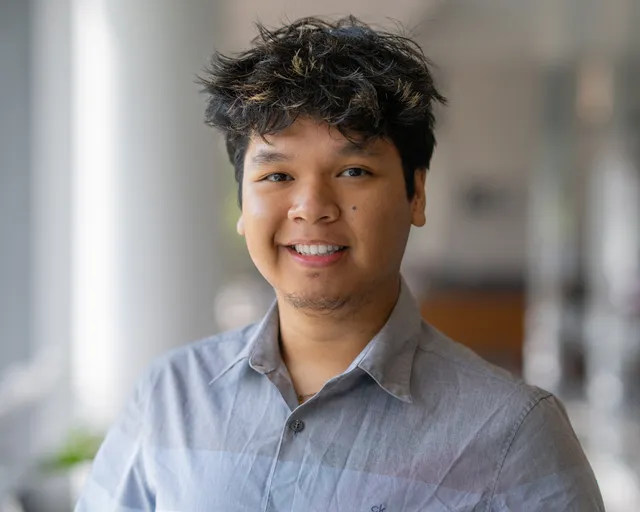 Headshot of Timothy Navarro smiling in a light blue collared shirt, in a bright columned hallway